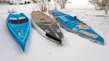 Fort Collins, CO, ABD - 25 Mart 2023: Kürek ve yarış sezonuna hazırlanmak - Sancak tarafından üç stand-up raket tahtası ve SIC Maui 'nin karla kaplı arka bahçesinde.