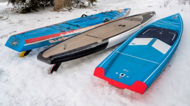 Fort Collins, CO, ABD - 25 Mart 2023: Kürek ve yarış sezonuna hazırlanmak - Sancak tarafından üç stand-up raket tahtası ve SIC Maui 'nin karla kaplı arka bahçesinde.