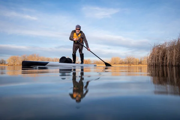 コロラド州の冬または早春の湖の上の彼のパドルボード上のシニアパドラー カエルの視点 部分的に水中アクションカメラ — ストック写真