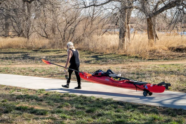 美国加利福尼亚州埃文斯市 2023年4月1日 身穿湿衣的老年男子皮划艇手正在用推车运送他的海上皮划艇 准备在科罗拉多州的南普拉特河早春划桨 — 图库照片