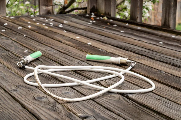 heavy fitness jump rope on a rustic, weathered wooden backyard deck in springtime scenery