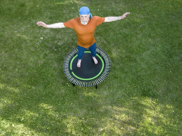 彼の裏庭のミニトランポリンで運動する高齢者の太りすぎ男性フィットネスとリバウンドの概念空中ビュー — ストック写真
