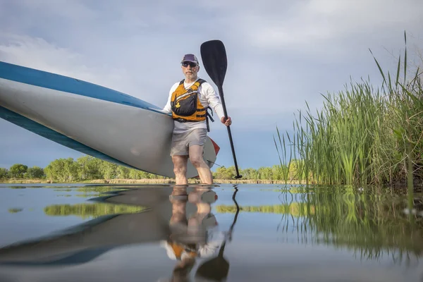 シニア男性パドラーは春に穏やかな湖の上にスタンドアップパドルボードを起動しています 水位でアクションカメラからカエルの視点 — ストック写真