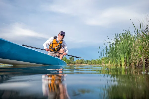 今年初春 年长的男子划桨手正在平静的湖面上划着一块独立的划桨板 这是从水位上的一个动作相机看到青蛙的 — 图库照片