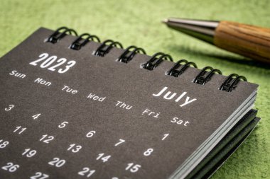 July 2023 - closeup of a small desktop calendar with a pen, time and business concept