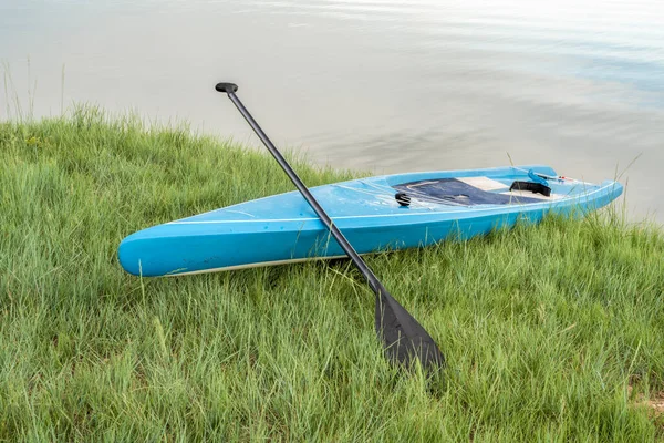 ツーリングスタンドアップパドルボード芝生の湖の海岸にパドル — ストック写真