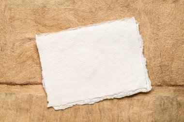 Toprak tonlarındaki soyut manzaraya karşı boş beyaz Khadi bez kağıtları.