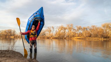 Mutlu son sınıf öğrencisi erkek kürekçi elinde şişirilebilir bir valizle bahar başlarında Kuzey Colorado 'da bir göl kıyısında kürek çekiyor.