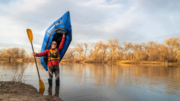在科罗拉多州北部的一个早春季节 快乐的老年男子划桨手拿着一只充气的皮划艇站在湖边划桨 — 图库照片