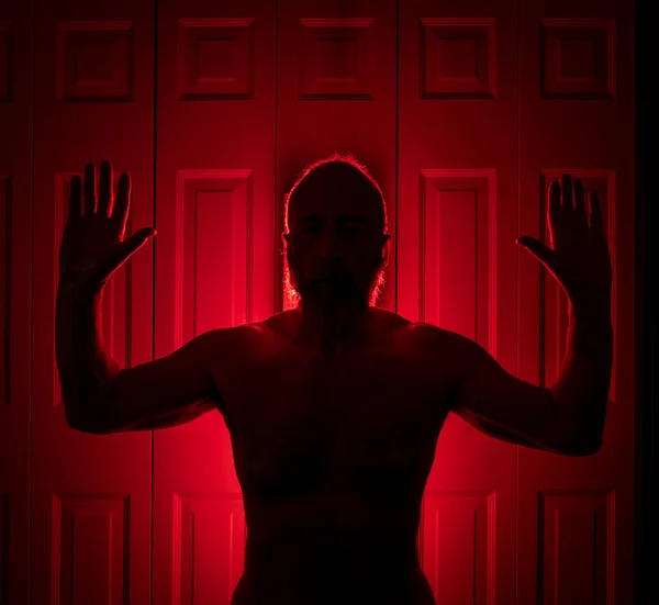 stock image silhouette of a senior athletic, man standing in front of the red light therapy panel in a bedroom