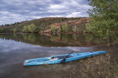 Fort Collins, CO, ABD - 16 Ağustos 2023: Hızlı tur stand up paddleboard düz su (2023 Waterline model) için tasarlanmış Horsetooth Reservoir at alacakaranlıkta seyir ışıkları açık.