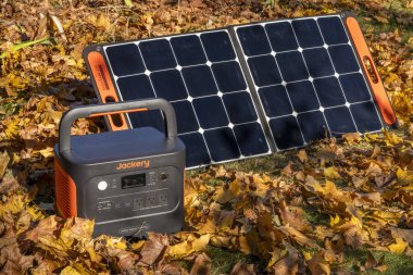 Fort Collins, CO, ABD - 5 Kasım 2023: Jackery Explorer 1000 + Portable Power Station, akçaağaç kuru yapraklarıyla kaplı bir alanda güneş paneli tarafından şarj ediliyor..