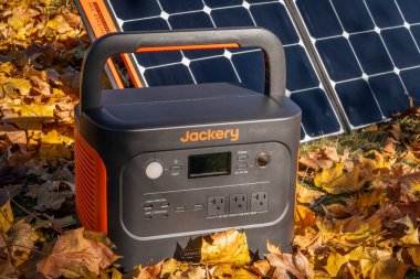 Fort Collins, CO, ABD - 5 Kasım 2023: Jackery Explorer 1000 + Portable Power Station, akçaağaç kuru yapraklarıyla kaplı bir alanda güneş paneli tarafından şarj ediliyor..