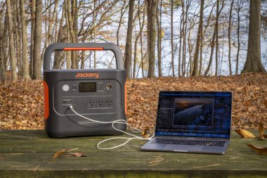 Colbert Ferry Park, AL, ABD - 23 Kasım 2023: Jackery Explorer 1000 + Taşınabilir Güç İstasyonu MacBook Pro bilgisayarını Tennessee Nehri kıyısındaki bir piknik masasında şarj ediyor.