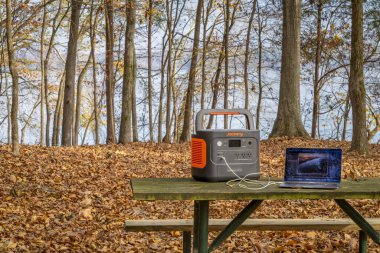 Colbert Ferry Park, AL, ABD - 23 Kasım 2023: Jackery Explorer 1000 + Taşınabilir Güç İstasyonu MacBook Pro bilgisayarını Tennessee Nehri kıyısındaki bir piknik masasında şarj ediyor.