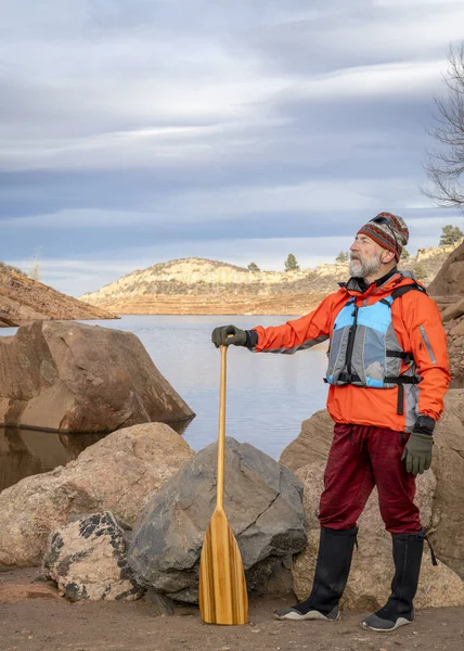 山の湖の岩岸に木製のカヌーパドルを持つ上級男性パドラー 秋や冬の景色のホースペース貯水池 — ストック写真