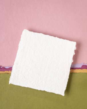 Hindistan 'dan gelen küçük beyaz Khadi bez kağıtları pembe ve yeşil pastel tonlarda soyut manzaralara karşı.