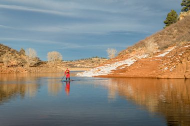 erkek paddler kırmızı drysuit paddleboard kadar bir stand Colorado, kış manzarası dağ gölde kürek çekmeye
