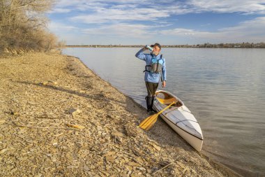 senior male paddler with expedition decked canoe on a lake shore in early spring, Boedecker Reservoir in northern Colorado clipart