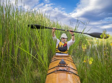 Colorado 'da bir gölde, sık kamışların arasından ahşap bir deniz kanosu inşa edilmiş bir evde kürek çeken yaşlı bir erkeğin yay görüntüsü.