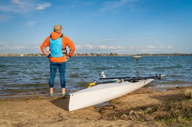 Senior male rower with his rowing shell on a beach of Boyd Lake in northern Colorado, early spring scenery clipart