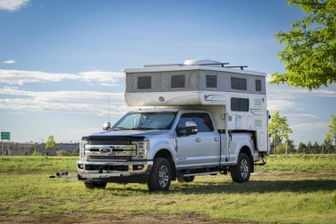 Loveland, CO, USA - August 25, 2024: Ford F350 truck with a pop up camper on a grassy area.