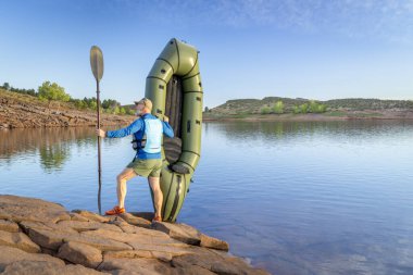 senior male paddler is launching an inflatable packraft on a shore of Horsetooth Reservoir in Colorado clipart