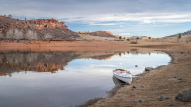 Kuzey Colorado 'da Horsetooth Rezervuarının kayalık sahilinde soğuk mevsim manzaralı ahşap bir kürek ile süslü bir keşif kanosu.