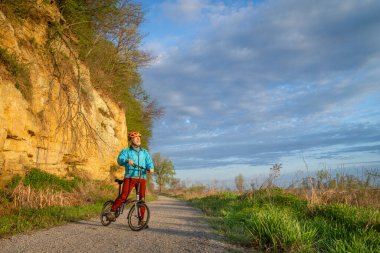 senior male cyclist riding a folding bike on Steamboat Trace, bike trail converted from an abandoned railroad, near Peru, Nebraska, springtime morning scenery clipart