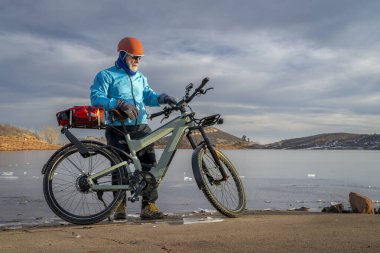Colorado eteklerindeki donmuş at dişi rezervuarının kıyısındaki gidona kamera monte edilmiş bisikletli son sınıf bisikletçi..