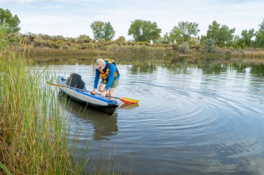 Son sınıf erkek kürekçi, sonbahar manzarasında Colorado 'da sakin bir gölde şişme bir kanoya biniyor..