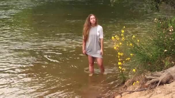 黄色の花の近くに灰色のドレスの彼を保持川に立つ白人ティーン女性 — ストック動画
