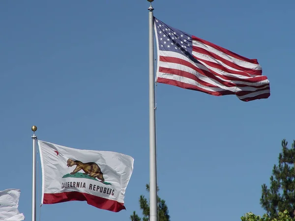 米国とカリフォルニア州の旗が青い空に向かって旗竿に掲揚 — ストック写真