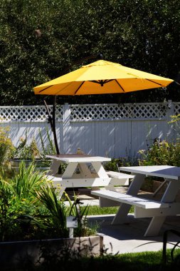 Beyaz piknik masaları ve sarı şemsiyeli Bahçe Bölgesi Davet Etme