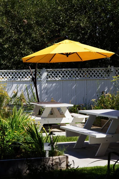 Beyaz piknik masaları ve sarı şemsiyeli Bahçe Bölgesi Davet Etme