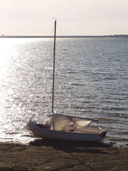 Small Sailboat With Sails Down But Mast Still Up On Beach Of Lake