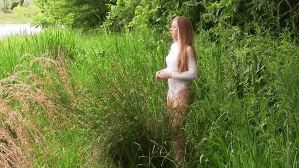 白衣を着た背の高い緑の草の中に立つ白人ティーンの女の子周りを見回す — ストック動画