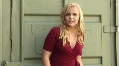 Young Caucasian Woman In Red Dress Standing And Posing In Front Of Green Metal Container