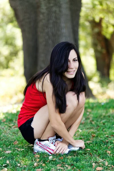 Attractive Latina Woman Squatting Outdoors Red Top Black Shorts Grass — Stock Photo, Image