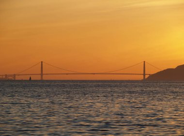 Körfez sularının karşısındaki Golden Gate Köprüsü 'nün uzak görüntüsü Orange Sunset Sky ile