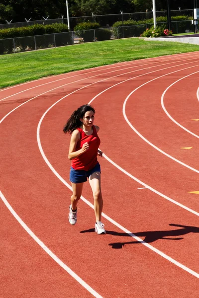 年轻的拉丁少女穿着红色上衣和蓝色短裤在跑道上奔跑 — 图库照片