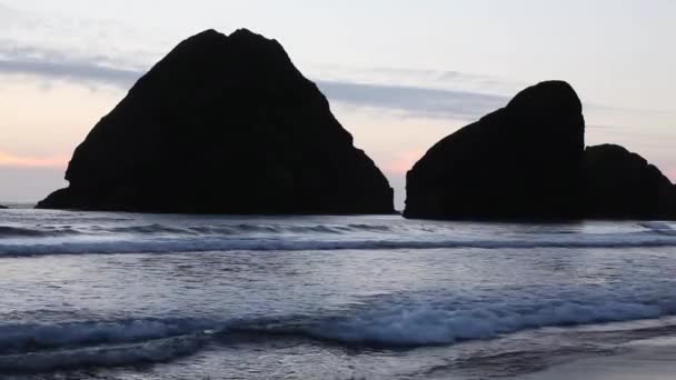 배경에 Siilhouetted 바위와 해변에 흐르는 — 비디오