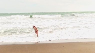 Bikini giymiş İspanyol bir kadın Kumsalda duruyor Soğuk rüzgarlar ve suda diz çökmüş dalgalarla