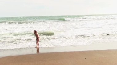Bikini giymiş İspanyol bir kadın Kumsalda duruyor Soğuk rüzgarlar ve dalgalar