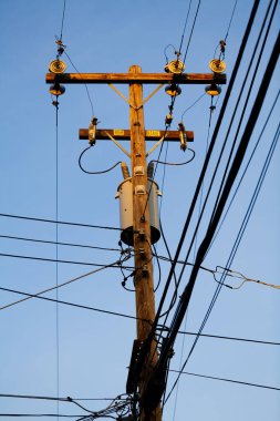 Tahta yüksek voltajlı elektrik direği. Mavi arkaplan ve dört yönlü birçok kablo var.
