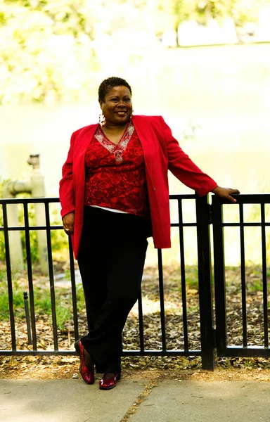 中年アフリカ系アメリカ人女性 屋外に立つ赤いトップと黒いパンツ 金属フェンスに保持 — ストック写真