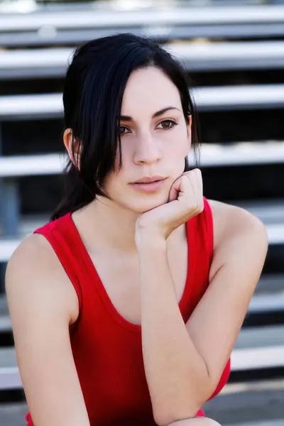 Young Attractive Slim Latina Woman Sitting On Bleachers In Red Top Head Resting On Hand