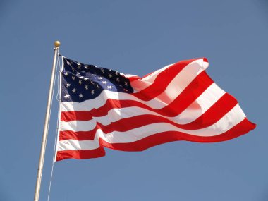 Açık mavi gökyüzünde bayrak direğinin tepesinde dalgalanan Amerikan bayrağının dar görüntüsü