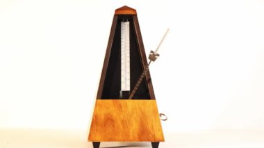 Orta hızda hareket eden ahşap metronom Tempo beyaz arka planda masada oturuyor.