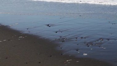 Deniz köpüğü ve küçük çakıl taşlarıyla kumsala vuran okyanus dalgaları.